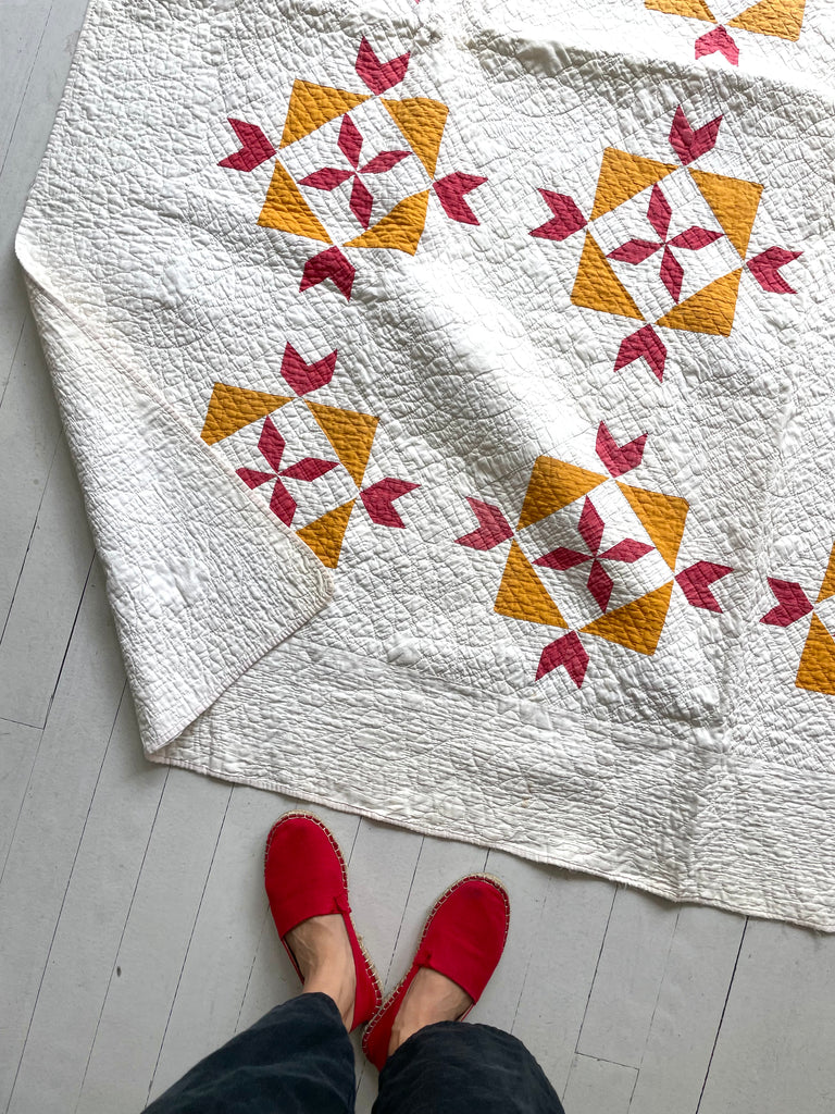 Quilt with star pattern on a white floor, person wearing red shoes partially visible